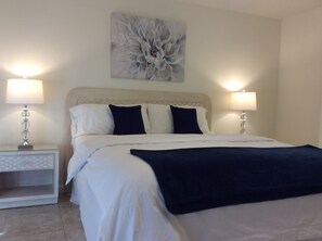 A neatly made bed with white and dark blue bedding, two bedside lamps, and a floral artwork above the bed. - Beautiful Condo at Mesquite Country Club -Pool, Hot Tub, Tennis (City ID:4337) (Palm Springs)