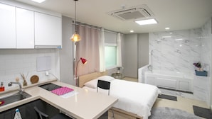 Una habitación de hotel moderna con kitchenette, una cama, un baño con bañera y una peque ña zona de estar.