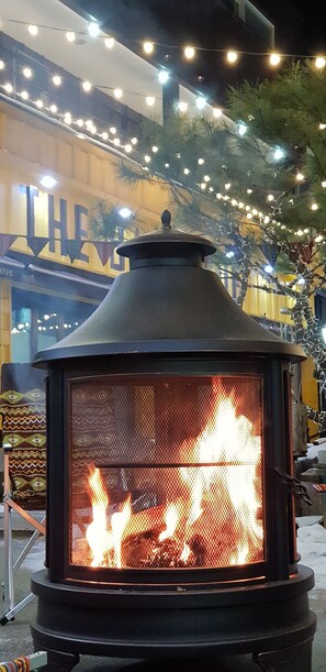 A wood-burning stove with a mesh front, surrounded by outdoor lights and greenery. - Blossom Pension (Gapyeong)