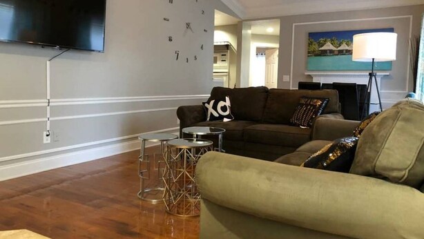 A living room with a sofa, a coffee table, and a TV mounted on the wall. - 6149 Sandcrest · Next TO Universal. 8 Beds. Pool. Very Clean (Orlando)