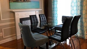A dining area with a glass table surrounded by chairs, a fireplace, and a painting of a tropical scene. - 6149 Sandcrest · Next TO Universal. 8 Beds. Pool. Very Clean (Orlando)
