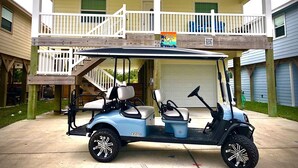 Une voiturette de golf est garée devant une maison à deux étages dotée d’un balcon.