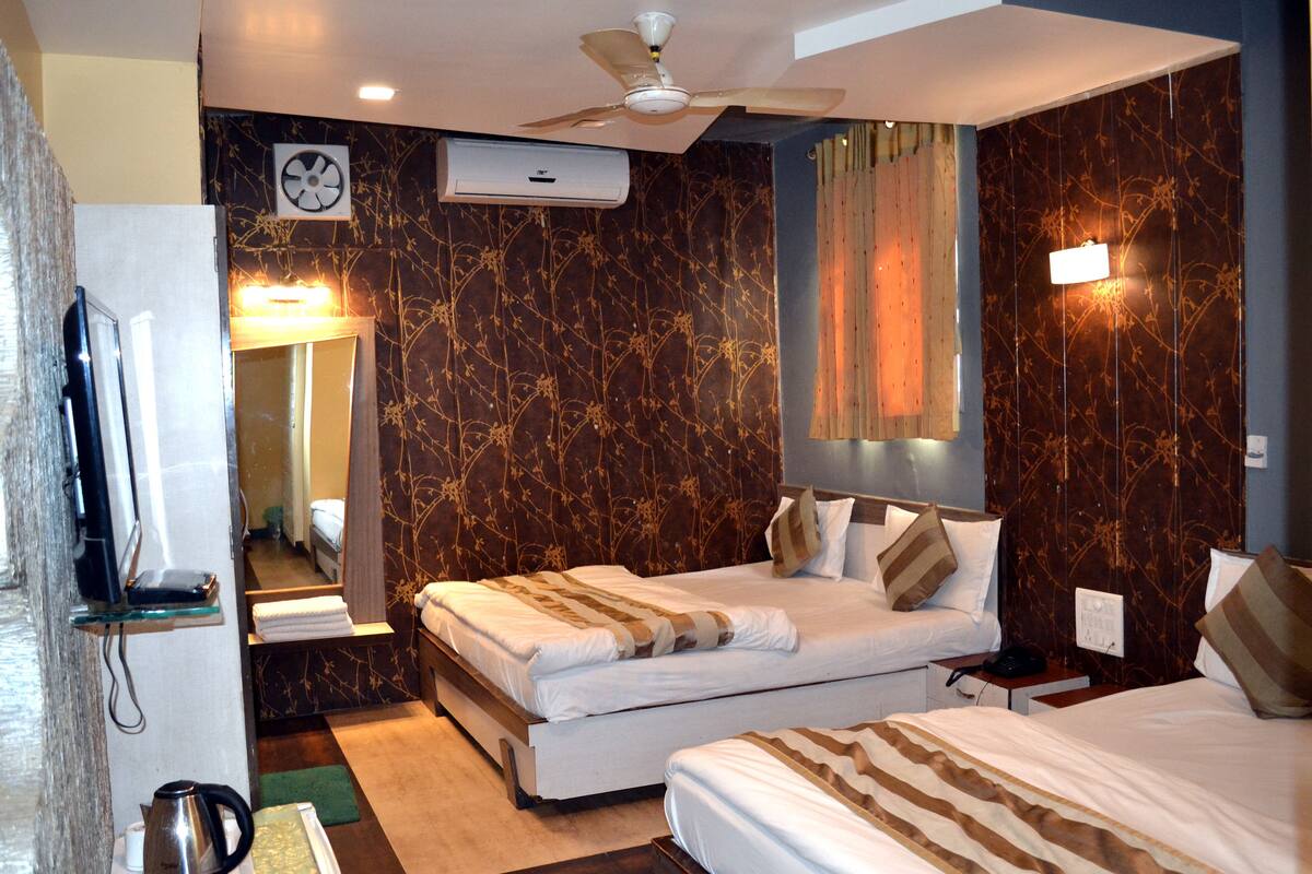 A hotel room with two beds, a ceiling fan, a TV, and a bathroom with a mirror and towel rack.