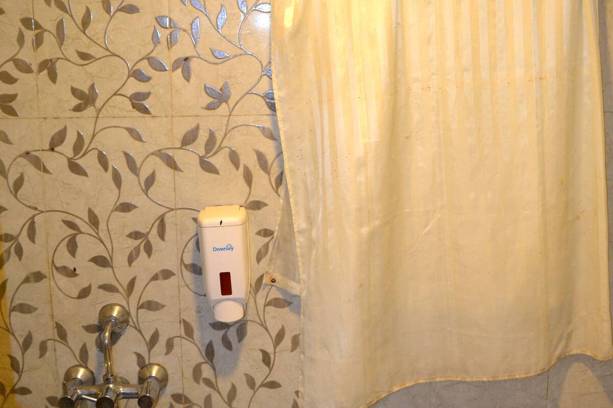 A bathroom with a floral tile pattern, a shower curtain, a soap dispenser, a toilet, and a blue and pink bucket.