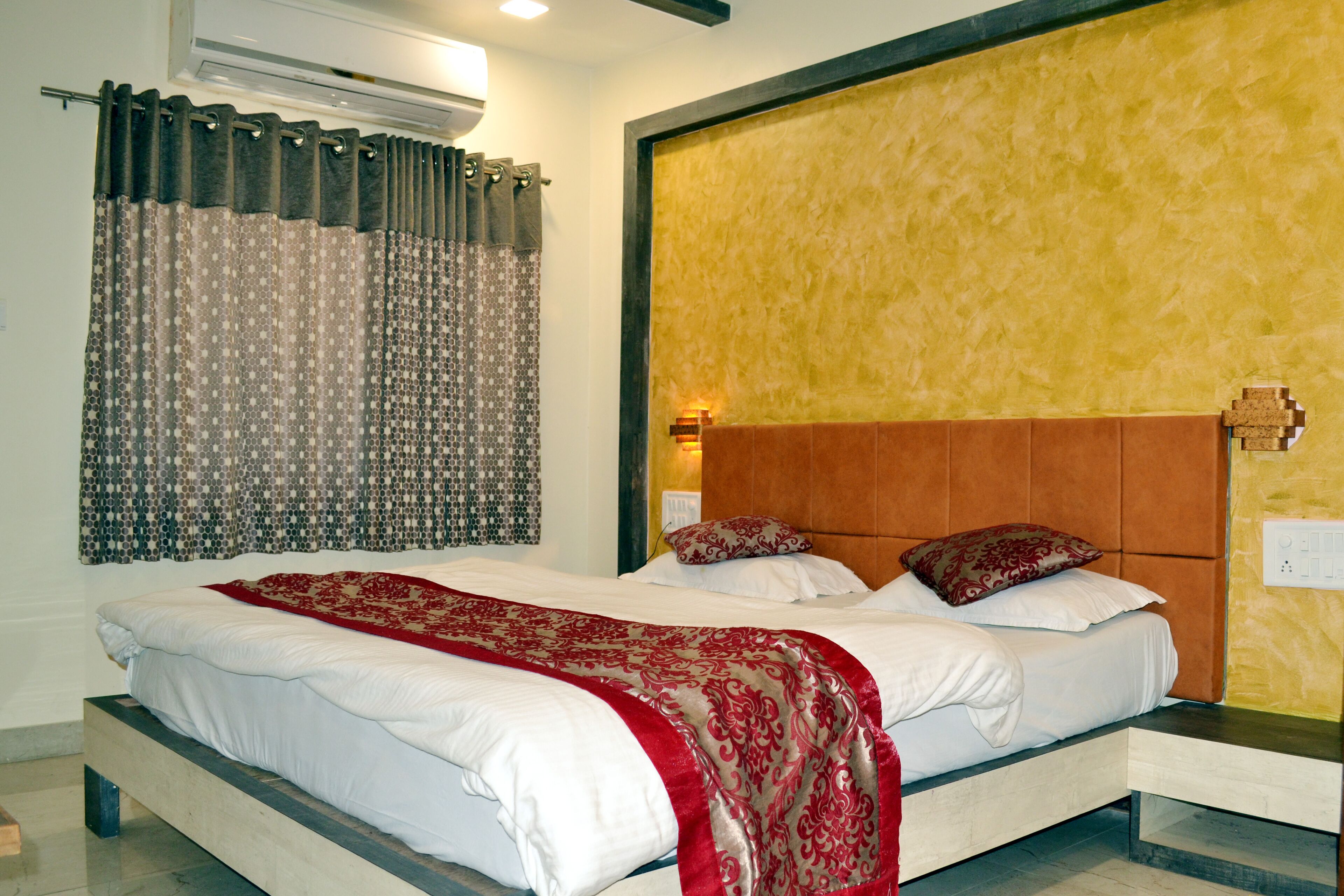 A bedroom with a bed, a nightstand, a wall-mounted light, and a window with curtains.