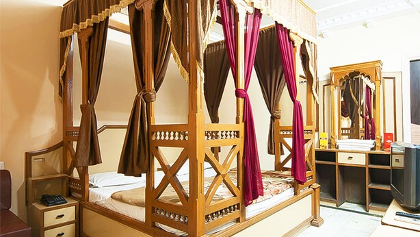 A four-poster bed with a wooden frame, a nightstand, a mirror, and a television on a stand. - Hotel Swagat (Abu Road)