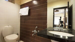 A bathroom with a white toilet, a sink with a mirror, and a towel hanging on the wall. - Hotel Swagat (Abu Road)