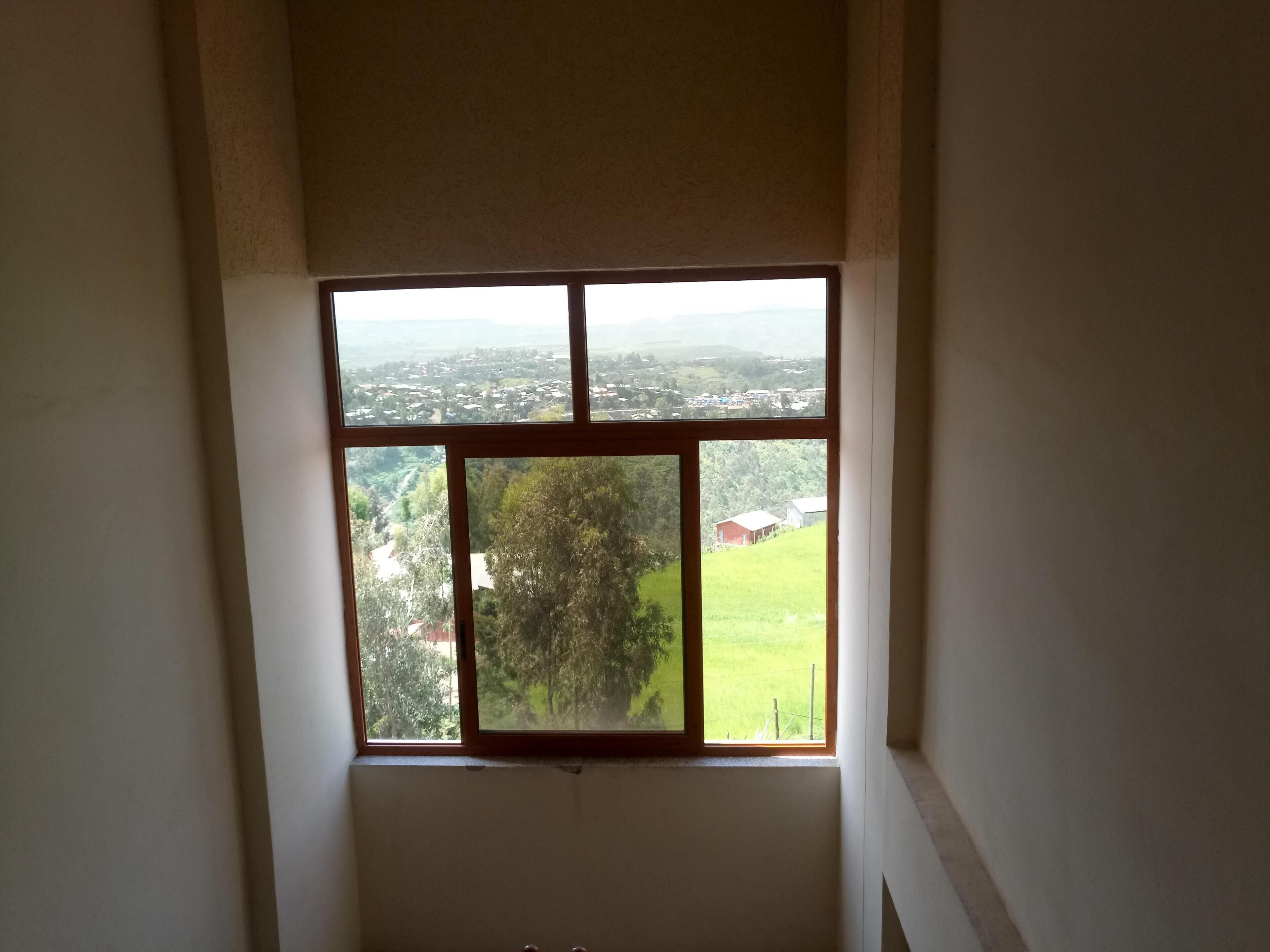 A room with a large window providing a view of a green landscape and distant buildings.