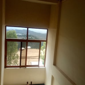 A room with a large window offering a view of a landscape with trees and distant hills. - Honey Land Hotel (Lalibela)
