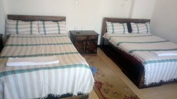 Two single beds with striped bedding, a small wooden nightstand, and a floral rug.