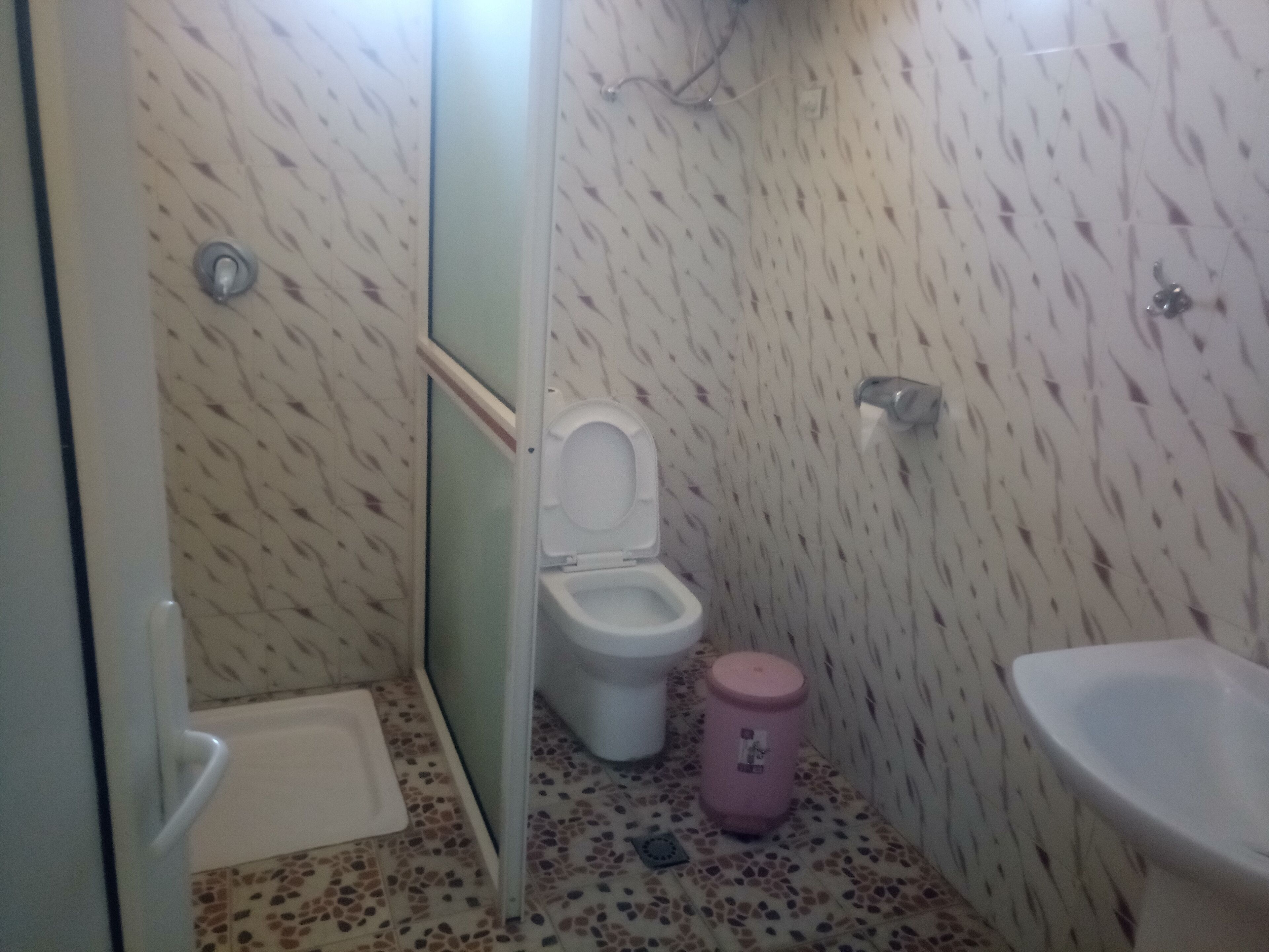Egy kis fürdőszoba, amelyben WC, mosdókagyló és zuhanyzó található.