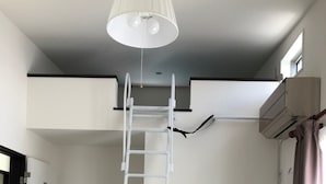 A white ladder in a room with a dark floor, a ceiling light, and an air conditioning unit. - SoraTerrace (Nishitokyo)
