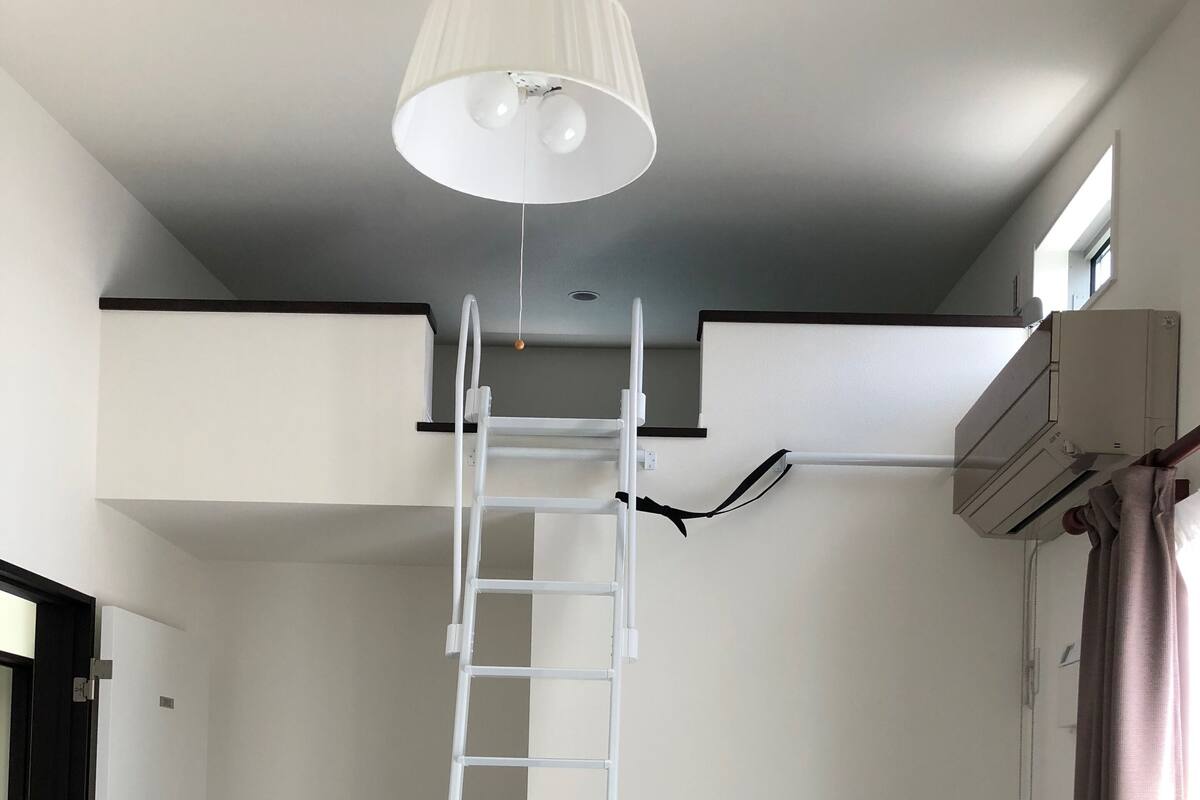 A white ladder in a room with a dark floor, a ceiling light, and an air conditioning unit.
