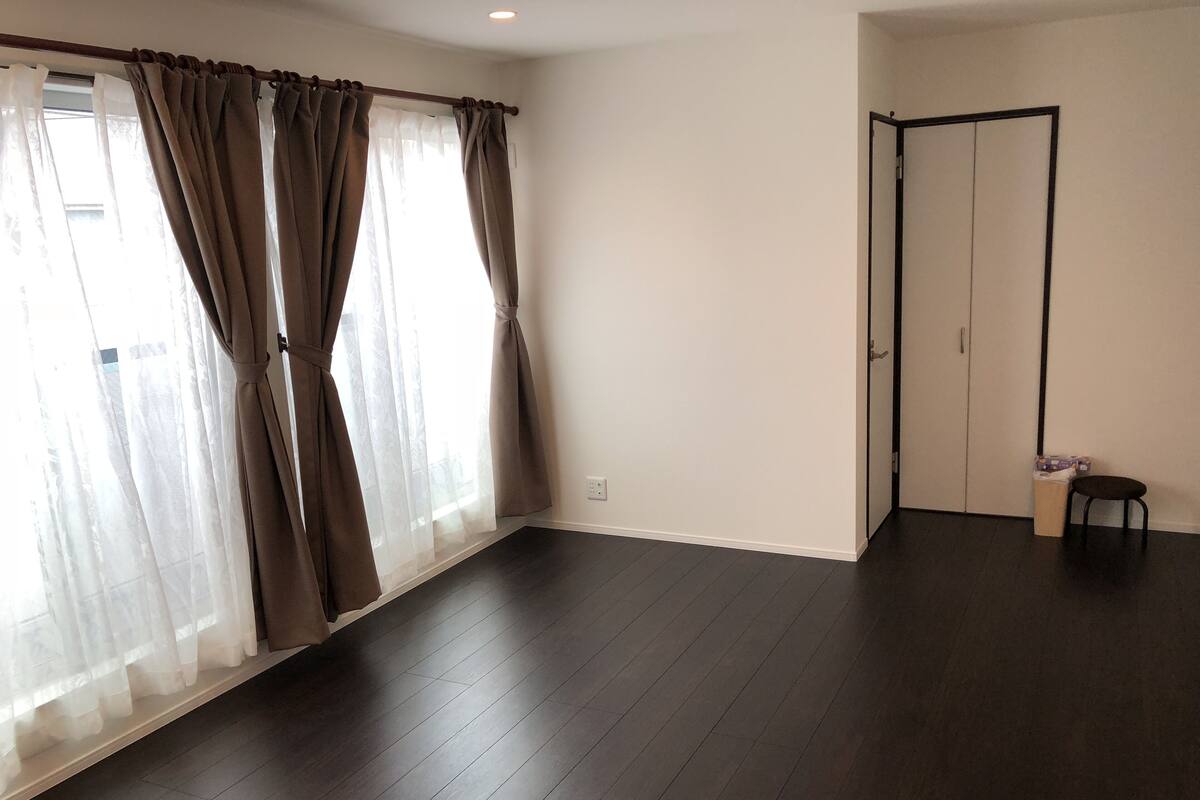 A room with a large window, dark wooden flooring, a door, and a small stool.