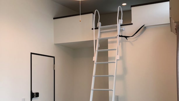 A room with a white ladder against a wall, a door with a black frame, and a ceiling light fixture. - SoraTerrace (Nishitokyo)