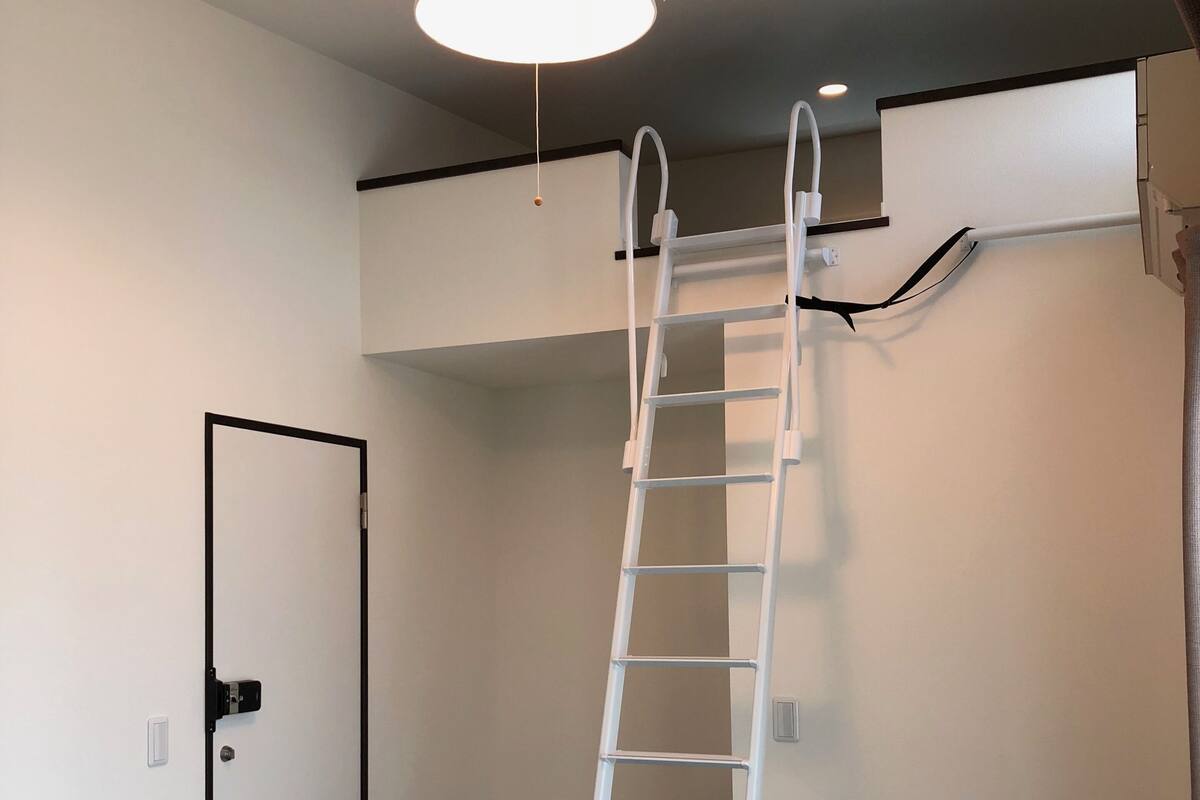 A room with a white ladder against a wall, a door with a black frame, and a ceiling light fixture.
