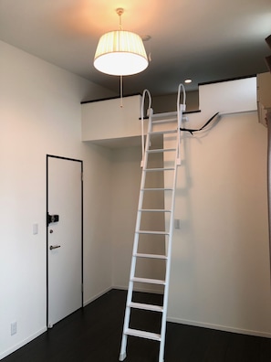 Ein Zimmer mit einer weißen Leiter an der Wand, einer Tür mit schwarzem Rahmen und einer Deckenleuchte.