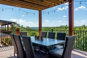 Un patio exterior con mesa y sillas, rodeado por una pérgola de madera y luces colgantes.