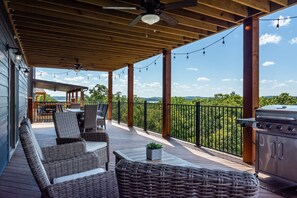 Terraza exterior techada con muebles de mimbre, una parrilla y luces colgantes.