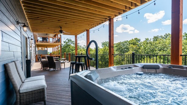 A wooden deck with a hot tub, outdoor seating, and a view of trees.