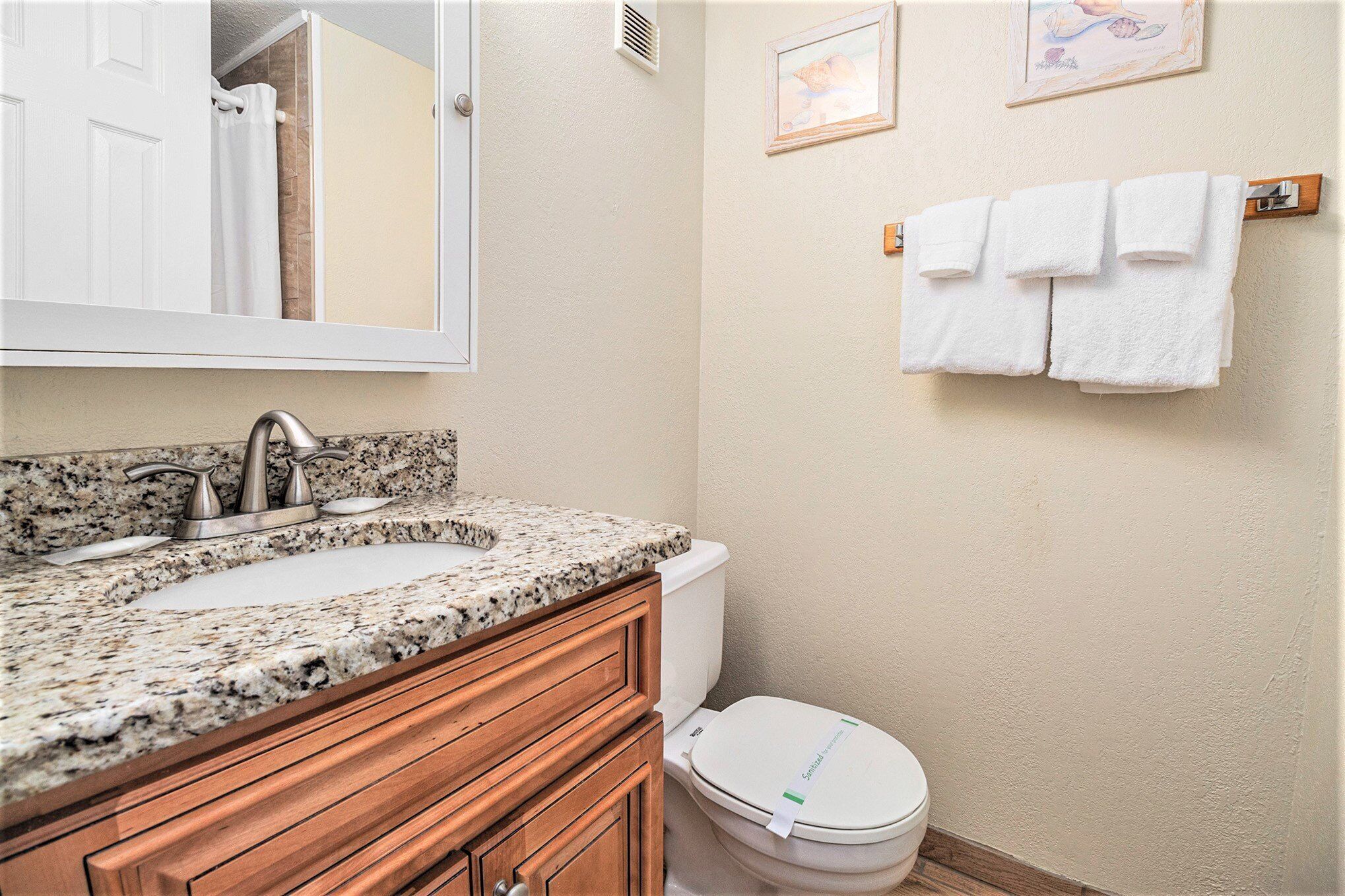 A bathroom with a granite countertop sink, wooden vanity, white toilet, and towels hanging on a rack.