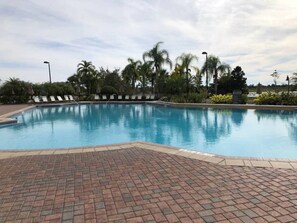 Piscina com deck de tijolos e espreguiçadeiras.