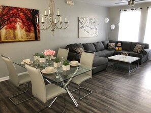 Ein modernes Wohnzimmer mit einem Glastisch, einem grauen Sofa und einem Deckenventilator.