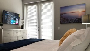 A bedroom with a bed, a TV mounted on the wall, a dresser, and a painting of a sunset. - Tideview 20 · Walk TO Convention! Near Universal & Disney (Orlando)