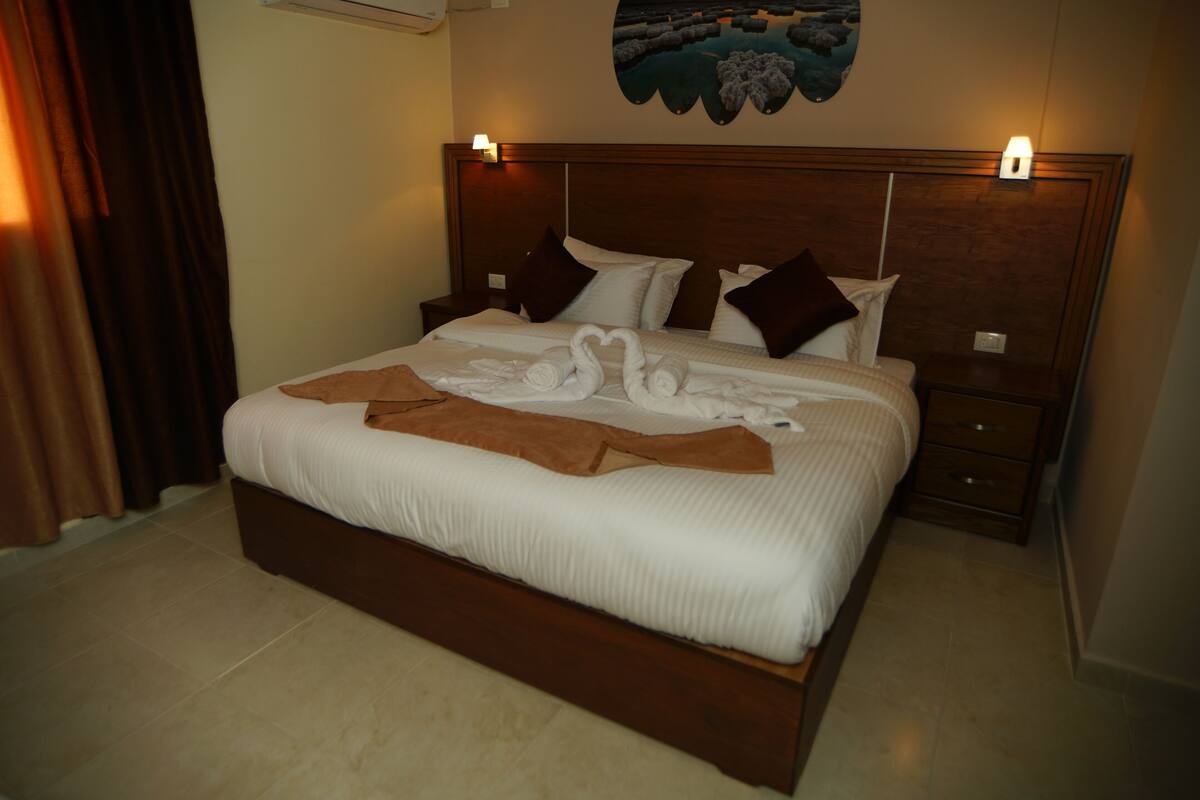 A neatly made bed with a brown throw blanket and two swan-shaped towels.