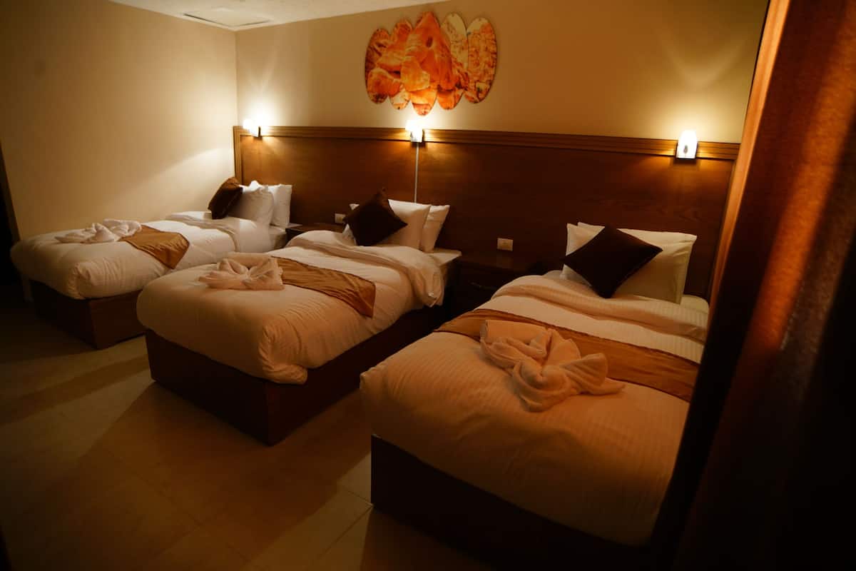 A hotel room with three beds, each with a wooden headboard, white linens, and brown throw blankets.