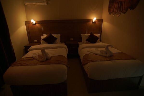 A hotel room with two beds, each with a wooden headboard, white linens, and towels. There are bedside lamps on either side of the headboard. - Petra Aretas Hotel (Wadi Musa)