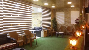 A modern indoor space with a green artificial turf floor, wooden ceiling with recessed lighting, and a variety of seating including wicker chairs and a sofa. - Petra Aretas Hotel (Wadi Musa)