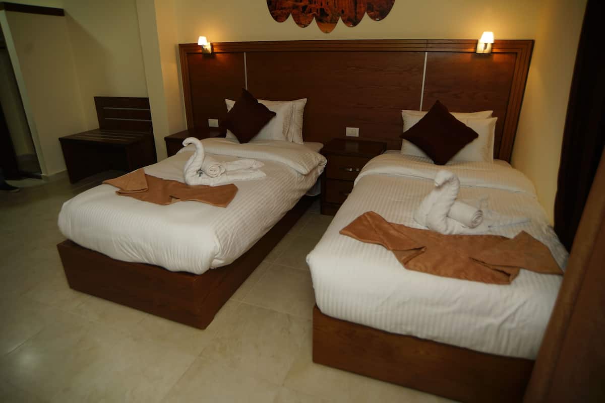 A hotel room with two beds, each with a wooden headboard and white bedding. There are brown towels on the beds and a wooden nightstand between them.