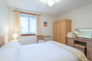 A bedroom with a bed, a desk, a chair, a wardrobe, and a window with curtains. - 2 Bed Home With Private Garden in the Highlands (Beauly)