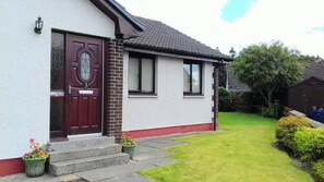 A single-story house with a red door, a brick chimney, and a small front garden. - 2 Bed Home With Private Garden in the Highlands (Beauly)