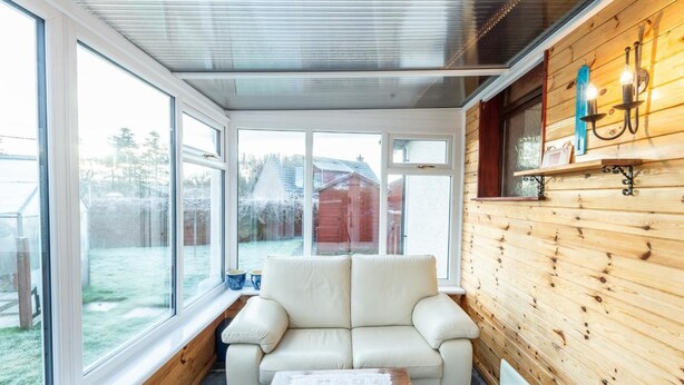 Una habitación acogedora con un sofá de cuero blanco, una pared de madera y ventanas amplias con vistas al jardín.