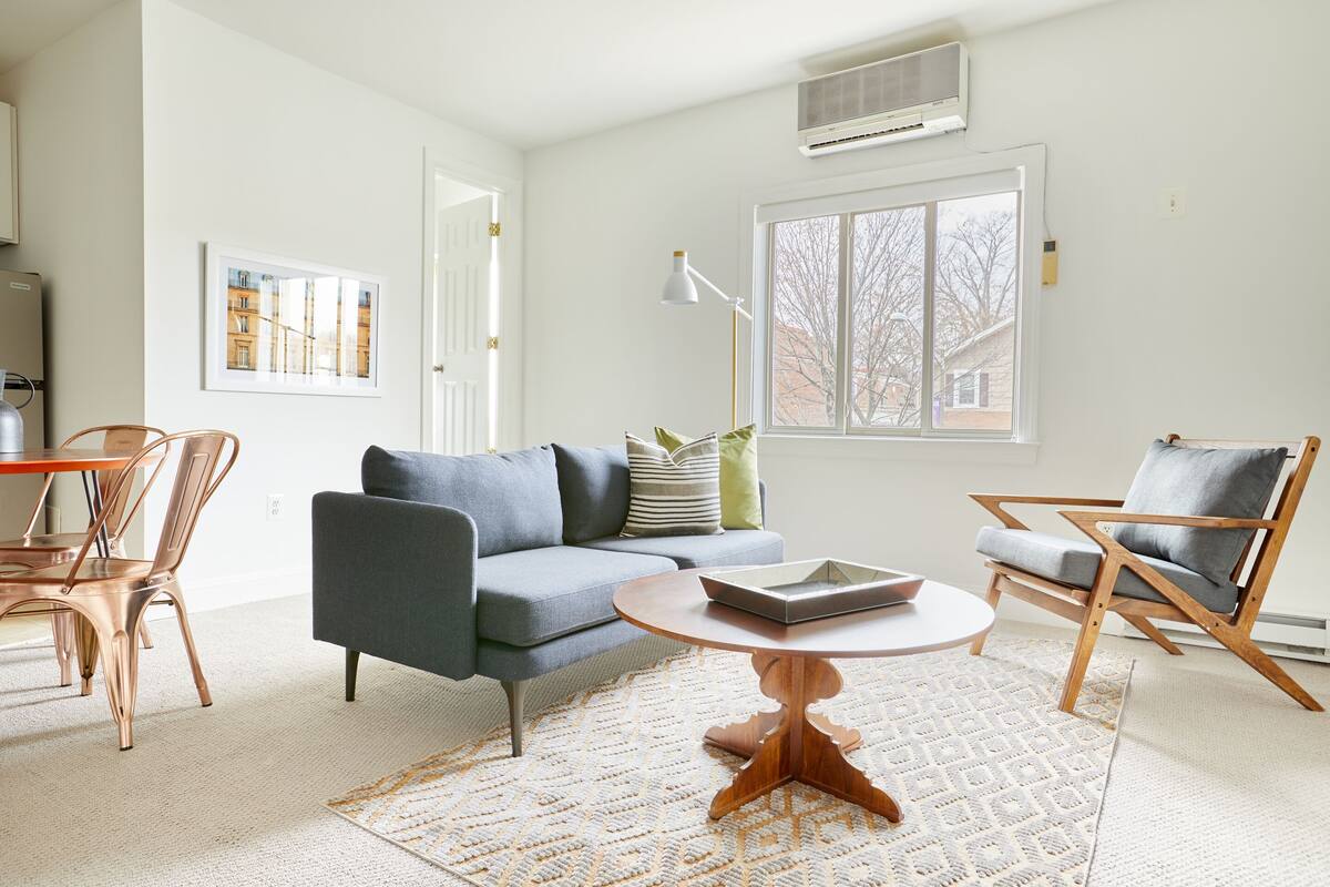Un salon moderne avec un canapé gris, des chaises en bois, une table basse ronde et un tapis à motifs.