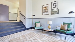 A modern living room with a staircase, two green upholstered chairs, a round coffee table, and a patterned rug. - Kasa Del Ray Alexandria (Alexandria)