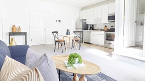A modern living room with a sofa, coffee table, and a dining area with chairs. - Kasa Del Ray Alexandria (Alexandria)