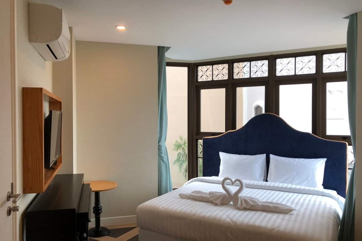 A hotel room with a large bed, a TV mounted on the wall, and a window with decorative iron bars.