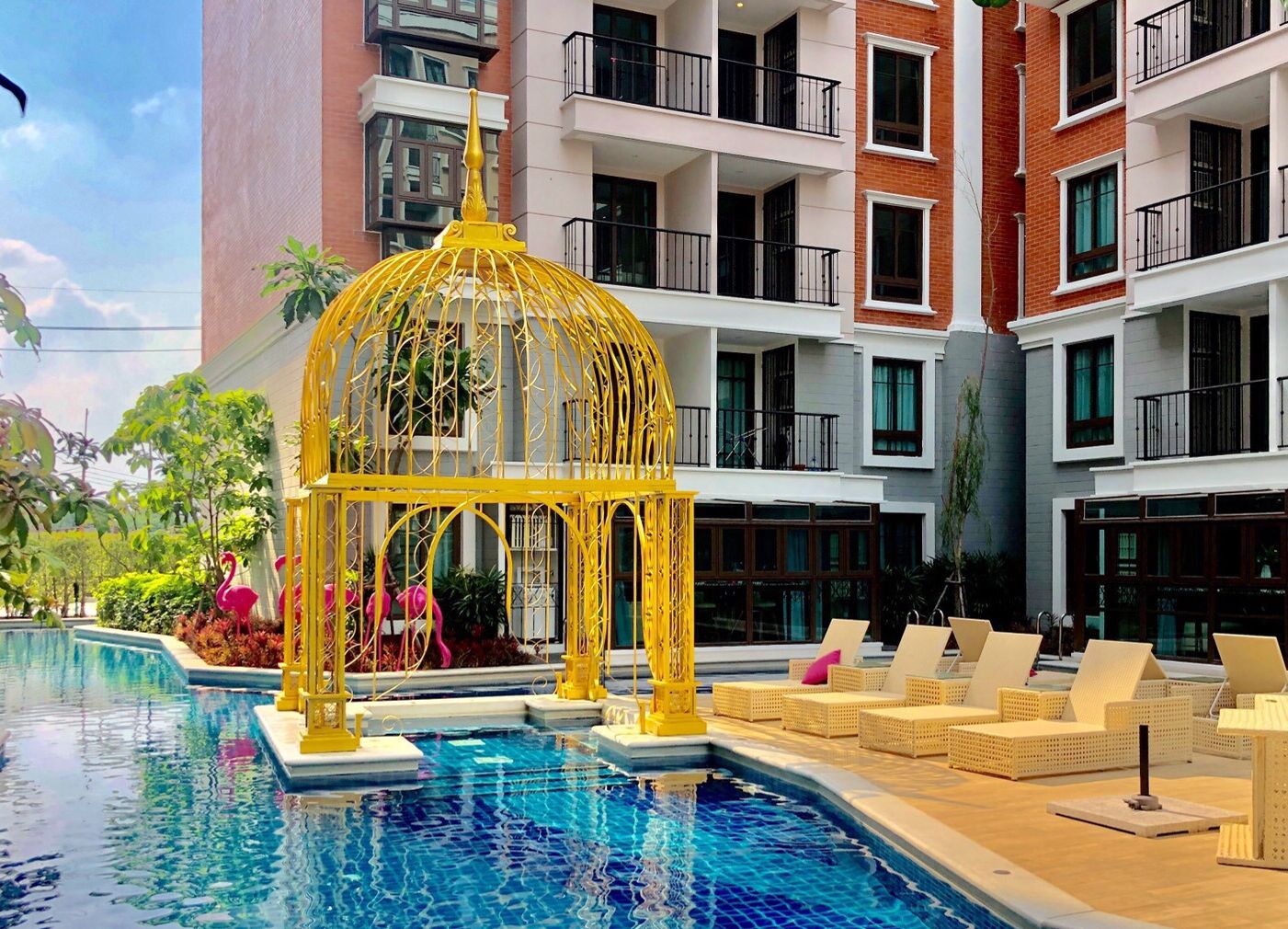 A swimming pool with a yellow gazebo, lounge chairs, and a multi-story building in the background.