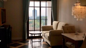 Un salon comprenant un canapé, une table à manger et offrant une vue sur un immeuble grâce à de grandes fenêtres.