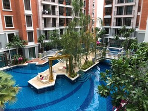 A large indoor swimming pool surrounded by lush greenery and a multi-story building with balconies. - Espana Condo Pattaya By JC (Pattaya)