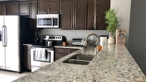 A kitchen with dark brown cabinets, stainless steel appliances, a granite countertop, and a potted plant. - Tideview 166 · NEW Ultra Modern & Super Clean 3 Full Suites (Orlando)