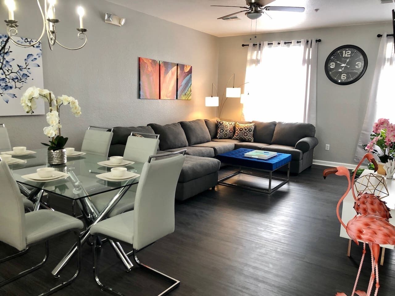 A modern living room with a glass dining table, grey sofas, and a blue coffee table.