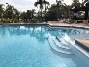 A clear swimming pool with steps leading into it, surrounded by palm trees and a covered seating area. - Tideview 166 · NEW Ultra Modern & Super Clean 3 Full Suites (Orlando)