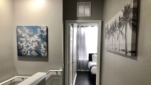 A hallway with a staircase, a bedroom with a bed and curtains, and artwork on the walls. - Tideview 166 · NEW Ultra Modern & Super Clean 3 Full Suites (Orlando)