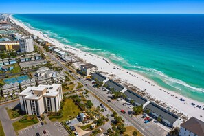 An aerial view of a coastal area with a beach, buildings, and roads.