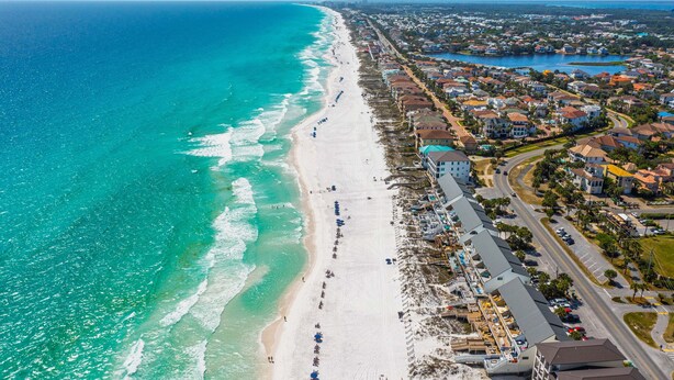An aerial view of a coastal town with a long beachfront, residential buildings, and a road parallel to the beach. - Beautiful Beachfront 4BR Green Reef townhome with Ocean Views! (Destin)