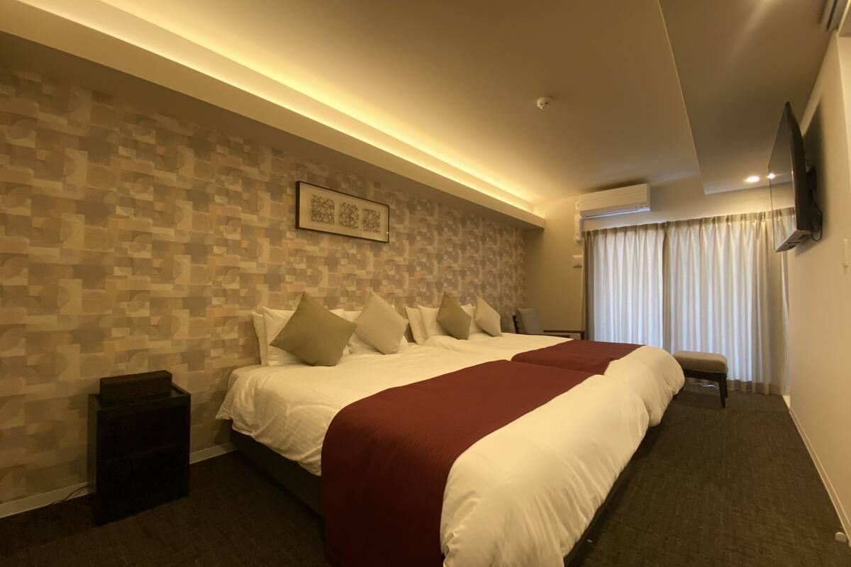 A modern hotel room with a large bed, a small table, and a TV mounted on the wall.